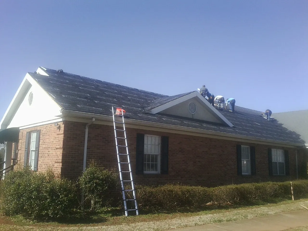 Crew tearing shingles off a brick ranch roof with a ladder set — Metal Roof Repair work by our crew in Macclesfield