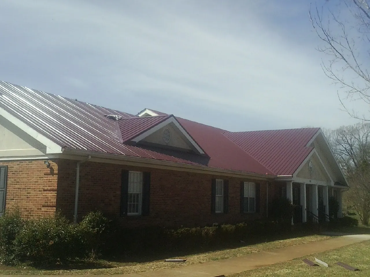 Red metal roof with gabled entries on a long brick building, from a Hail Damage Roof Repair job in Macclesfield