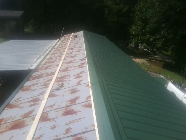 Old rusted panels beside newly installed green metal roofing — Wind Damage Roof Repair by Roofing Brothers in Macclesfield