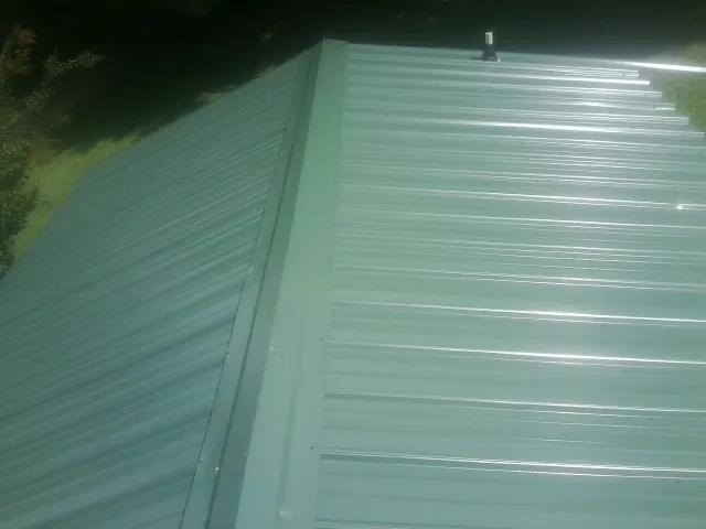 New green metal panels meeting at the ridge of a roof — Flat Roof Repair work by our crew in Macclesfield